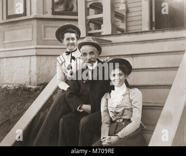 Antike ca. 1905 Foto, Vater und zwei erwachsenen Töchtern auf der Treppe ihres Hauses sitzen. Lage unbekannt, wahrscheinlich New England, USA. Ich habe weitere Fotos von dieser Familie in Riggsville, Maine, USA. Stockfoto