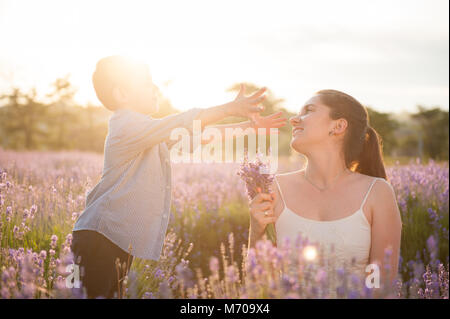 Gerne nette Junge möchte zu umarmen, Mom und erreicht Ihr mit offenen Armen unter Blumenwiesen im Sommer Stockfoto