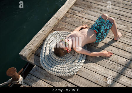 Junge mit Sonnenbrille Sonnenbaden im Sommer Sonne liegen auf alten hölzernen Pier Stockfoto