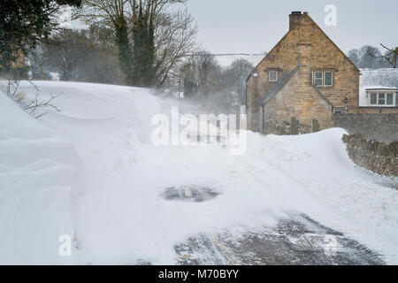 Schneeverwehungen auf der anderen Straßenseite in Snowshill Dorf im März. Snowshill, Cotswolds, Gloucestershire, England Stockfoto