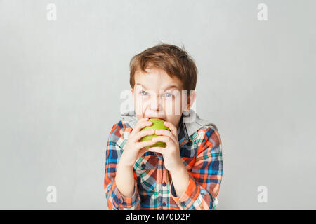 Junge beißt eine Green Apple in einem karierten Hemd, auf grauem Hintergrund Stockfoto