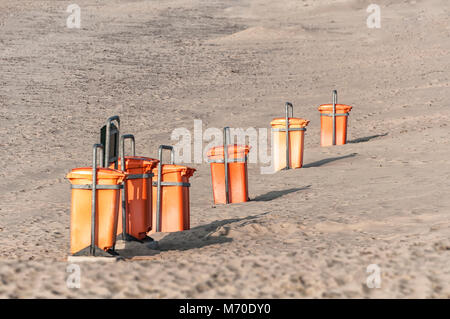 Orange Mülleimer in einer Reihe stehen am Strand Stockfoto