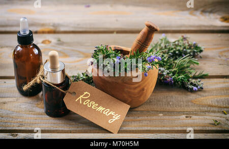 Rosemary wesentliches Öl und frischen blühenden Zweig in einem hölzernen Mörtel, Holztisch, Variable mit Text Rosmarin Stockfoto