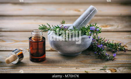 Rosemary wesentliches Öl und frischen blühenden Zweig in einem Stein, Mörtel, Holz- Tabelle Stockfoto