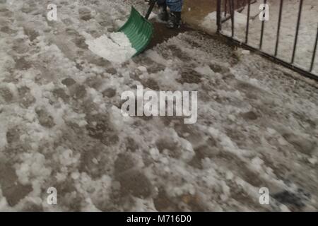 Schaufeln ein Bürgersteig in Matschigen Schnee während der Nor'easter März 7th, 2018 in Brooklyn, New York. Stockfoto