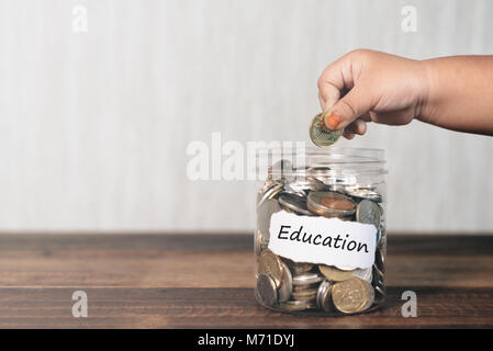 7/8 Hand ein Kleinkind die Münze in jar voller Münzen, Speichern für Bildung Konzept Stockfoto