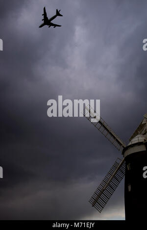 Thaxted Essex England. Flugzeug Landung am Flughafen Stansted über John Webb's Mühle erbaut im Jahre 1804 fliegen. März 2018 Sturm, Wolken und Regen approc- Stockfoto