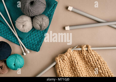 Grau und Türkis stricken Wolle und Stricken auf Stricknadeln auf beigem Hintergrund. Ansicht von oben. Platz kopieren Stockfoto