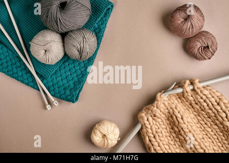 Grau und Braun stricken Wolle und Stricken auf Stricknadeln auf beigem Hintergrund. Ansicht von oben. Platz kopieren Stockfoto