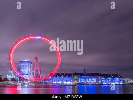 Das London Eye und der County Hall leuchtet rot und blau an einem bewölkten November Abend. Stockfoto