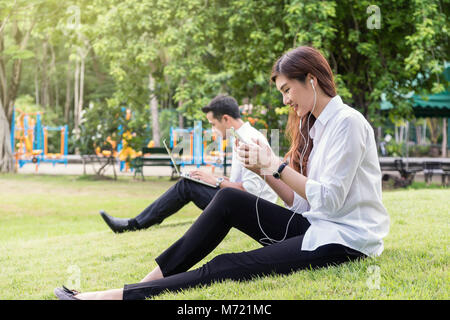 Gerne asiatische Paar hören das Lied über smart phone Kamera und mit dem Laptop im Park, Liebhaber und Lifestyle Konzept Stockfoto