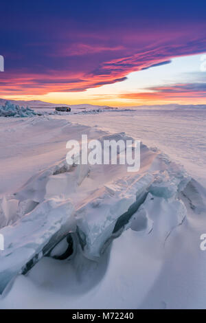 Winterlandschaft im Sonnenuntergang, gerissene gefrorenen See bedeckt von Schnee am Baikalsee in Russland mit schönen Sonnenuntergang Himmel Stockfoto