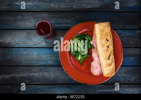 Lecker Sandwich mit Schinken, Pilzen und grünem Salat auf einer Keramikplatte. Farbige Holz- Hintergrund. Ansicht von oben Stockfoto