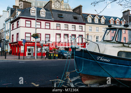 Cobh, Irland - 9 November, 2017: malerischen Blick auf die Promenade von kleinen irischen Stadt mit dem Boot auf die Vorder- und die traditionellen Geschäfte auf Hintergrund Stockfoto