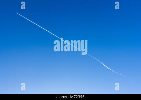 Flugzeug in den blauen Himmel lässt weiße Streifen hinter ihm. Die Richtung ist diagonal. Es kann als Hintergrund verwendet werden. Platz für Text. Stockfoto