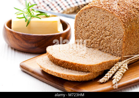 Langsam geschnitten - gebackene Bio Vollkorn Brot mit Butter und Rosmarin und Weizenähren Stockfoto