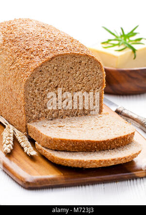 Langsam geschnitten - gebackene Bio Vollkorn Brot mit Butter und Rosmarin und Weizenähren Stockfoto