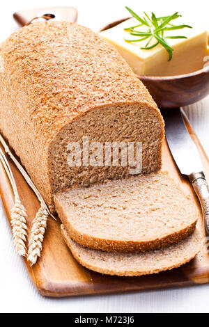 Langsam geschnitten - gebackene Bio Vollkorn Brot mit Butter und Rosmarin und Weizenähren Stockfoto