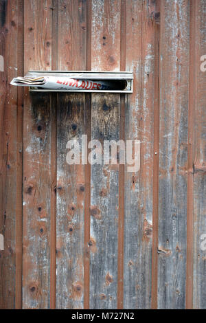 Ein Steckplatz mit einer gelieferten Zeitung in eine alte Holztür. Stockfoto