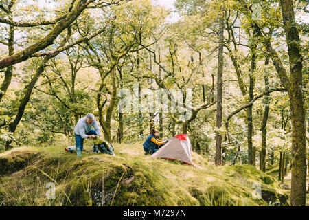 Ältere Paare haben ihren Platz in der Woodlands entschieden sich für wildes Campen. Die Frau ist die Einrichtung des Zeltes und der Mann wird immer Dinge aus Stockfoto