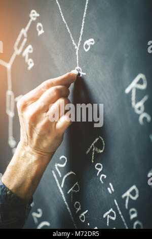 Der Lehrer schreibt an einer Tafel mit Kreide eine Formel für elektrischen Strom. Stockfoto