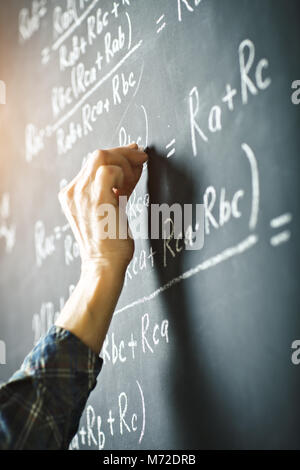 Der Lehrer schreibt an einer Tafel mit Kreide eine Formel für elektrischen Strom. Stockfoto