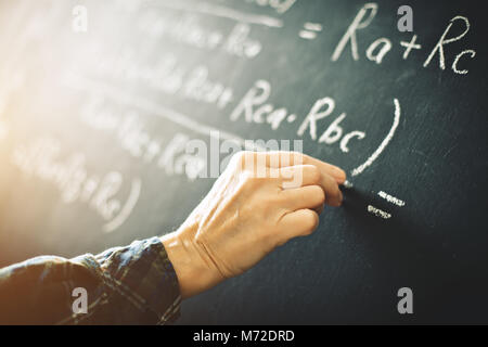Der Lehrer schreibt an einer Tafel mit Kreide eine Formel für elektrischen Strom. Stockfoto