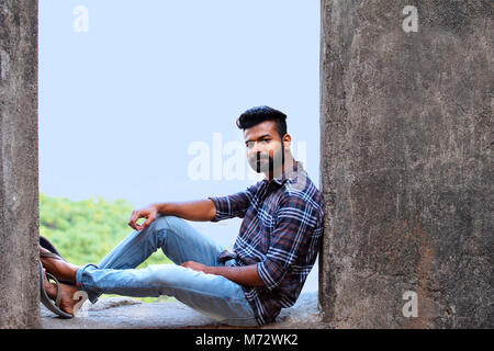 Männliches Modell sitzen auf einem Felsvorsprung an der Kamera suchen, Sion fort, Mumbai, Maharashtra Stockfoto