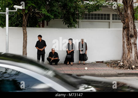 Vier Menschen in schwarzer Kleidung, stehen auf dem Bürgersteig der Straße in Ratchadamnoen Straße während der Trauer für Ende der thailändische König Bhumibol Stockfoto