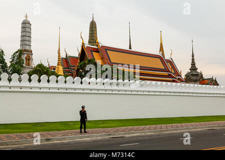 Silhouette eines thailändischen Polizisten gegen die weiße Wand des Grand Palace, mit dem Tempel und Stupas im Hintergrund Stockfoto