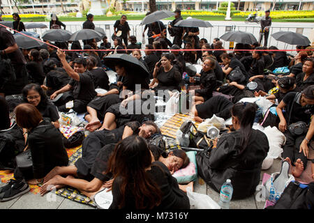 Masse der Leute auf dem Bürgersteig in der Ratchadamnoen Road in Bangkok, dem Tag der Königlichen Feuerbestattung. Frauen sitzen und schlafen in ihren schwarzen Kleidern Stockfoto