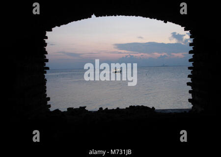 Westerly Blick von Fort Jefferson in der Abenddämmerung. Im Bau von 1846 bis 1875, das Fort wurde nie vollendet. Die große Öffnung hier gesehen hätte einen embrasyre Für eine Geschützstellung gewesen, aber Untergang der Fort alle Arbeiten in der zweiten Ebene im Jahr 1865 angehalten. Durch die Öffnung sichtbar ist der Dry Tortugas Licht auf Unechte in der Ferne, und ein einsames Schiff im Vordergrund. Man kann sich vorstellen, den Blick auf ein feindliches Kriegsschiff aus diesem Blickwinkel, und die den Ruf zu den Waffen hören wie gun Crew für die Verteidigung. Dieses Fischereifahrzeug martime, wie seine Vorgänger, der sicheren Uhr gesucht Stockfoto