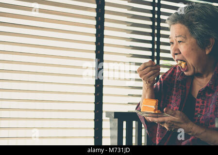 Elder senior Essen orange Kuchen im Cafe. Die asiatischen ältere Frau sitzen und köstliche Dessert im Restaurant. Stockfoto