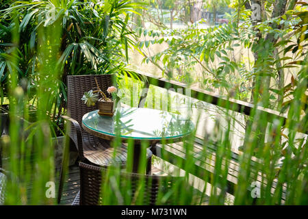 Runde Holz Tisch auf der Terrasse des Hauses. wicker rattan Stuhl auf der Terrasse in der Nähe von Garten zu Hause. entspannten lifestyle Konzept. Stockfoto