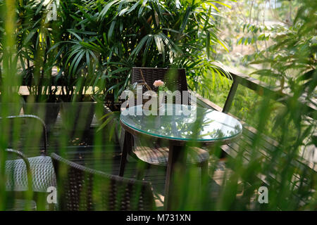 Runde Holz Tisch auf der Terrasse des Hauses. wicker rattan Stuhl auf der Terrasse in der Nähe von Garten zu Hause. entspannten lifestyle Konzept. Stockfoto