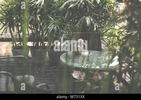 Runde Holz Tisch auf der Terrasse des Hauses. wicker rattan Stuhl auf der Terrasse in der Nähe von Garten zu Hause. entspannten lifestyle Konzept. Stockfoto