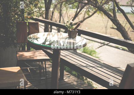 Runde Holz Tisch auf der Terrasse des Hauses. wicker rattan Stuhl auf der Terrasse in der Nähe von Garten zu Hause. entspannten lifestyle Konzept. Stockfoto