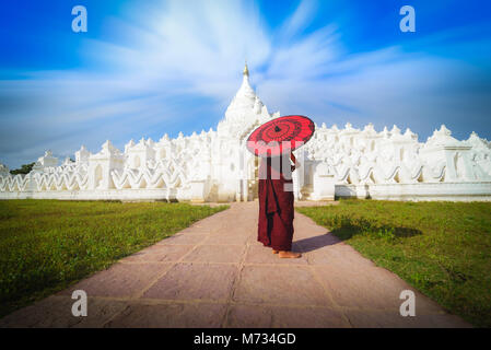 Asiatische junge Mönch halten roten Sonnenschirme am blauen Himmel in der Mya Thein Tan Mingun Pagode in Mandalay, Myanmar. Stockfoto