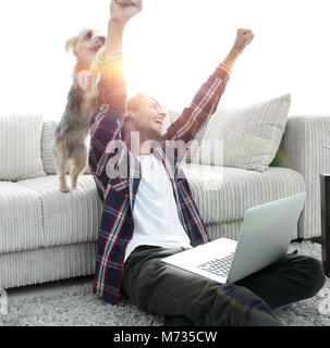 Happy Guy frohlockt mit seinem Hund sitzt in der Nähe der Couch im Wohnzimmer. Das Konzept der häuslichen Leben Stockfoto