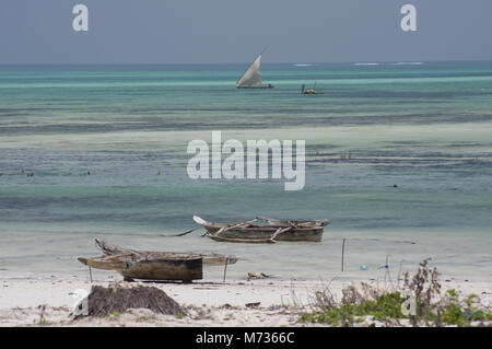 Die türkisblauen Wasser des Indischen Ozeans bei Ebbe mit Strände boote Dhaus, im Vordergrund und ein Segelboot im Hintergrund Sonne und Sand Stockfoto