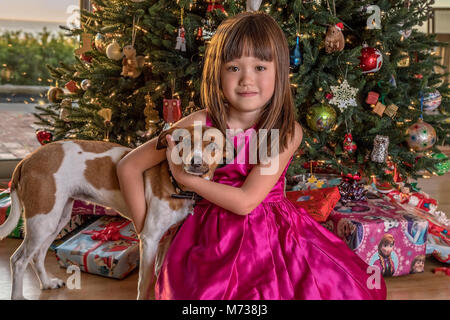 Fünf Jahre altes Mädchen und ihr Hund sitzt unter dem Weihnachtsbaum Stockfoto