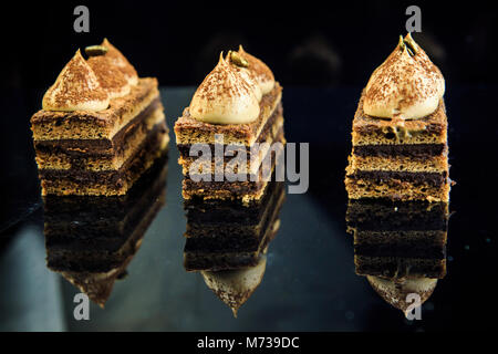 Leckere Schokolade Oper Kuchenscheiben mit weißer Creme auf Black Mirror Hintergrund eingerichtet Stockfoto