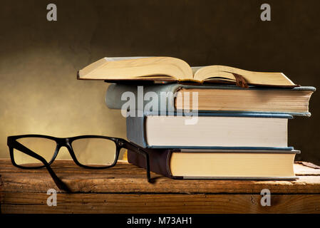 Öffnen Sie Buch mit Lesebrille auf dem dunklen Hintergrund Stockfoto