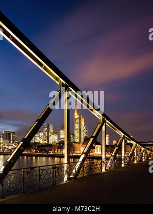 Skyline von Frankfurt am Main, Deutschland, durch die stählernen Trägern der "Eiserner Steg" Fußgängerbrücke über den Main in der Abenddämmerung gesehen. Stockfoto
