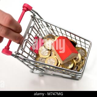 Ein kleines Haus in einer Miniatur Einkaufswagen mit einem Pfund Münzen Haus Konzept kaufen Stockfoto