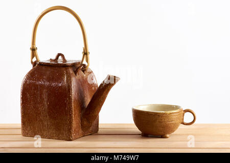 Teekanne und Tasse Tee auf einem Holztisch, auf weißem Hintergrund Stockfoto