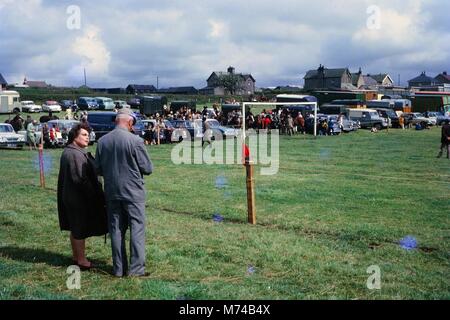 Die Menschen haben ihre Autos geparkt und versammelten sich um einen abgesperrten Bereich um einen Wettbewerb mit Pferden, 1965 zu beobachten. () Stockfoto