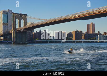 New York, NY, USA: ein Paar auf einem jetski Rennen entlang des East River unter der Brooklyn Bridge auf einem sonnigen Herbst Tag in New York. Stockfoto