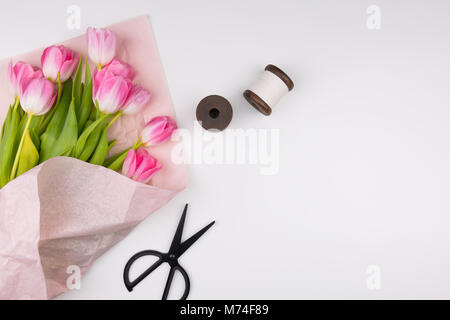 Minimal styled flat lay with pink tulips flowers with petals in pink paper wrapper, two thread spools and black scissors. Mock up top view. Stockfoto