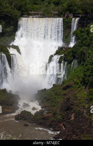 Erhöhte panorama Iguazu Wasserfälle Wasserfälle mit Perspektive entfernten winzigen Touristen auf Gehweg trail UNESCO Weltnaturerbe Naturwunder der Welt Stockfoto